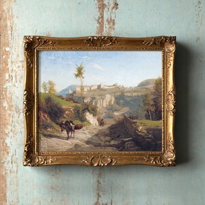 A rustic landscape painting in an ornate gold frame hangs on a textured, light blue wall. It depicts a serene rural scene with hills and a donkey.
