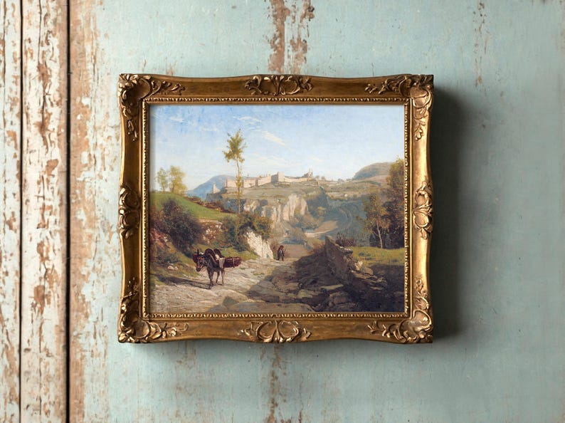 A rustic landscape painting in an ornate gold frame hangs on a textured, light blue wall. It depicts a serene rural scene with hills and a donkey.