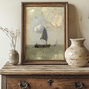 A framed painting of a sailboat on calm seas sits on a rustic wooden dresser. Beside it are two ceramic vases, one with dry branches, in a serene, vintage setting.