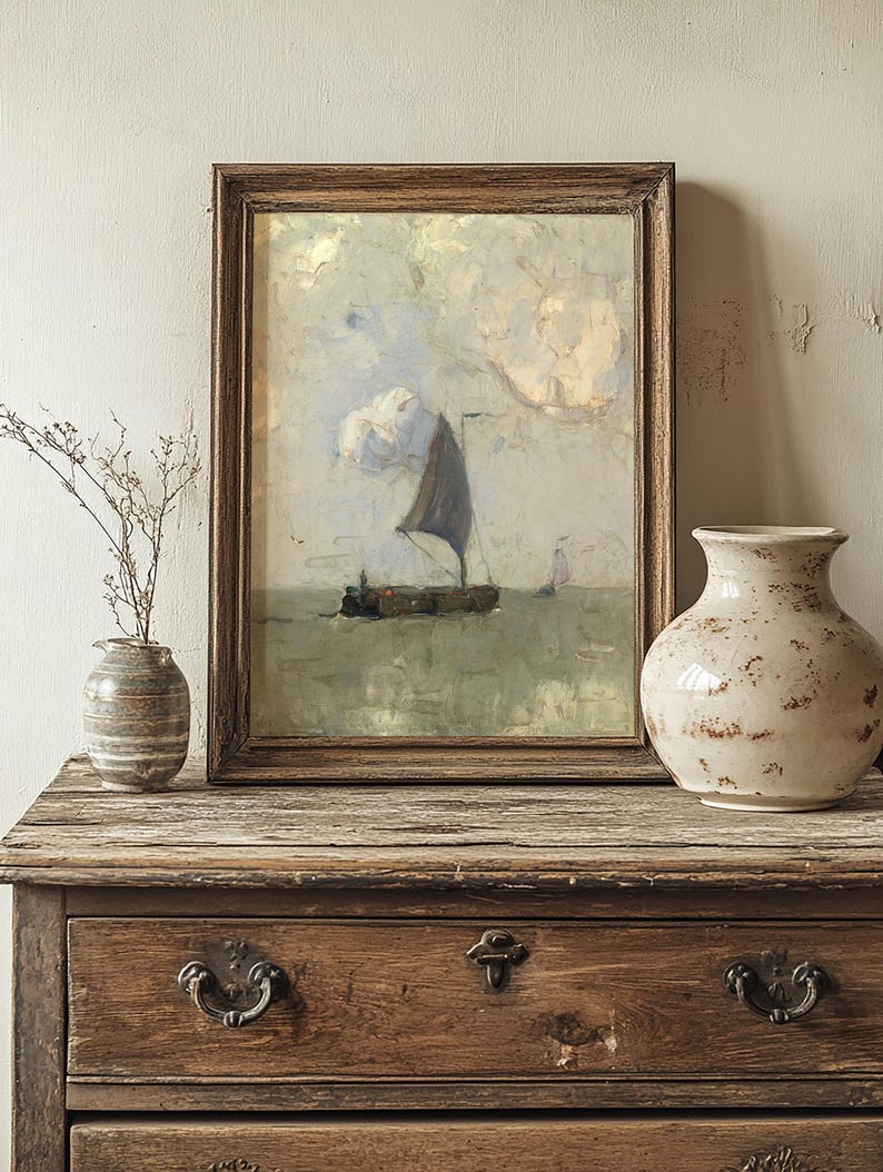 A framed painting of a sailboat on calm seas sits on a rustic wooden dresser. Beside it are two ceramic vases, one with dry branches, in a serene, vintage setting.