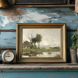 Framed landscape painting of a countryside with trees and a cottage, set against a distressed blue wall. Nearby, an antique clock and potted plants add a rustic feel.
