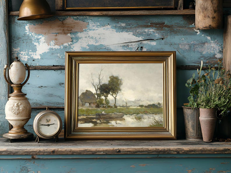 Framed landscape painting of a countryside with trees and a cottage, set against a distressed blue wall. Nearby, an antique clock and potted plants add a rustic feel.