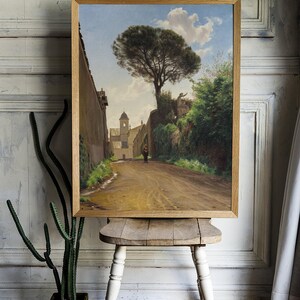 A framed painting depicting a narrow, dirt road leading to a church with a tall pine tree in the foreground. The road is lined with stone walls and lush greenery. A single figure walks along the road, adding a sense of scale and perspective to the scene.