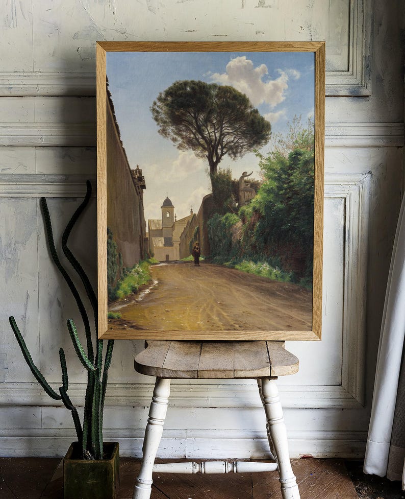 A framed painting depicting a narrow, dirt road leading to a church with a tall pine tree in the foreground. The road is lined with stone walls and lush greenery. A single figure walks along the road, adding a sense of scale and perspective to the scene.