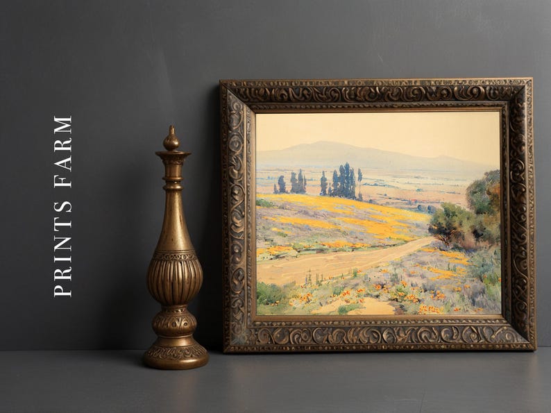 Framed landscape painting of a rolling countryside with yellow flowers and distant trees, next to an intricately carved bronze vase on a gray background.