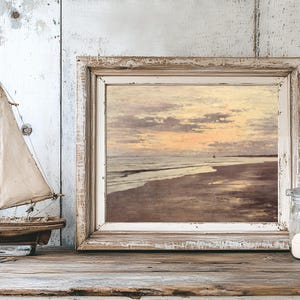 A rustic wooden table holds a framed seascape painting with a sunset, next to a small model sailboat and a jar of sand, evoking a tranquil beach vibe.