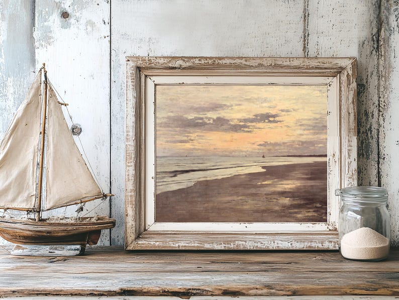 A rustic wooden table holds a framed seascape painting with a sunset, next to a small model sailboat and a jar of sand, evoking a tranquil beach vibe.