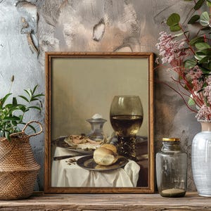 Framed still life of a meal with wine is on a wooden shelf. A woven basket with greenery and a gray vase with pink flowers flank it on either side.