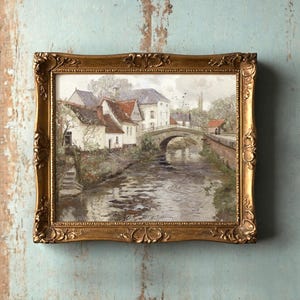 Framed painting of a serene village scene with a stone bridge over a river, surrounded by quaint houses and soft greenery, exuding a tranquil ambiance.