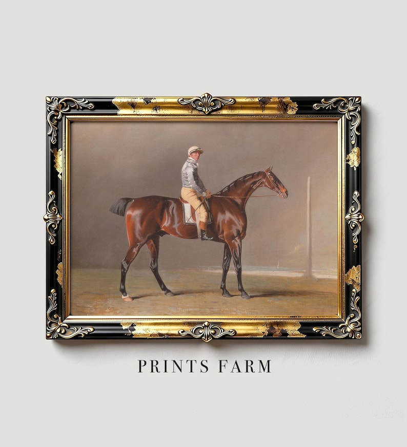 Framed painting of a jockey on a brown horse in a black and gold ornate frame. Neutral background with "PRINTS FARM" text below. Classic, elegant tone.