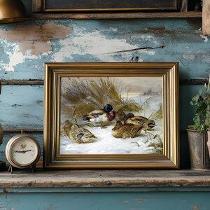 A rustic shelf displays a painting of ducks on a snowy landscape, framed in gold. Beside it, an antique clock and a vintage lamp, with plants to the right.