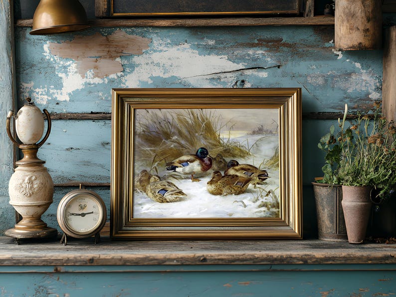 A rustic shelf displays a painting of ducks on a snowy landscape, framed in gold. Beside it, an antique clock and a vintage lamp, with plants to the right.