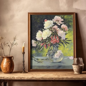 A framed painting of vibrant peonies in a vase, set on a rustic wooden table with a copper pot, dried flowers, a candle, and an aged ceramic jar.