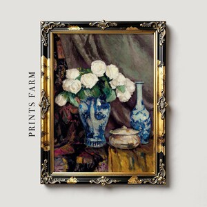 Framed painting of white roses in a blue vase, accompanied by a matching blue bottle and a small dish, set against a draped fabric background.