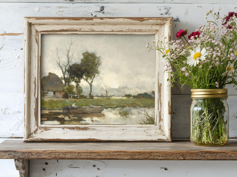 Framed landscape painting of a serene lake with trees and a cottage, next to a jar of wildflowers on a rustic wooden shelf, creating a tranquil, rustic vibe.