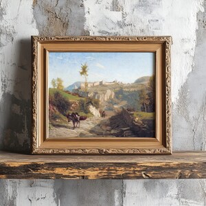 A framed landscape painting on a rustic wooden shelf against a textured wall. It depicts a scenic path with a donkey, leading to distant hills.