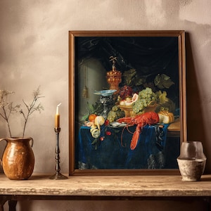 A framed still-life painting on a wooden shelf depicts a lavish spread of fruit and a lobster on a blue cloth. Nearby, a candle, pottery, and a small vase.
