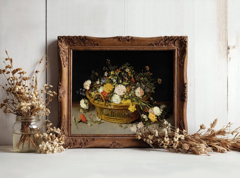 A framed painting of a basket filled with colorful flowers, set against a dark background. Rustic wood frame, surrounded by dried flowers on a white surface.