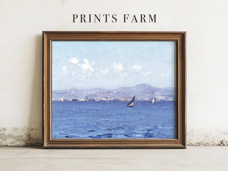 A framed seascape painting leaning against a wall, featuring a sailboat on a calm blue sea with mountains and clouds in the background. The words "PRINTS FARM" are above it.
