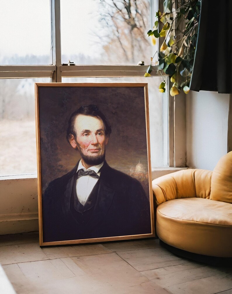 A framed portrait of a bearded man in a suit leans against a window with a scenic view. Nearby, a cozy yellow chair adds warmth to the setting.