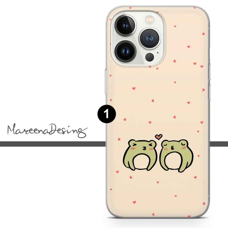 Op de afbeelding: Een transparante telefoonhoes met een lichtroze achtergrond en een patroon van kleine rode hartjes. Twee groene kikkers bevinden zich in het midden van de hoes en kijken elkaar aan. De kikker links heeft zijn mond open en de kikker rechts heeft zijn ogen dicht. Het nummer "1" bevindt zich in de rechterbovenhoek van de hoes.