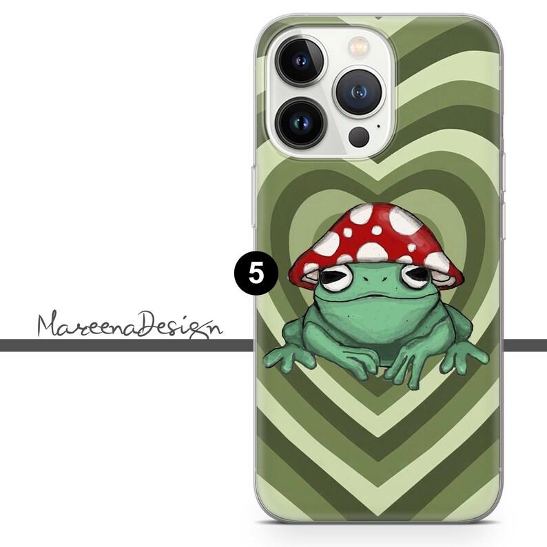 Op de afbeelding: Een groene kikker met een rode en witte paddenstoelhoed zit in een hart op een groen-wit gestreepte telefoonhoes. De telefoonhoes heeft een transparante achterkant en een verhoogde camerabult.