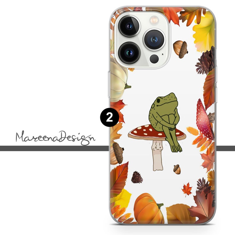 Op de afbeelding: Een transparante telefoonhoes met een witte achtergrond en een kleurrijk herfstbladerenontwerp. Een groene kikker zit op een rode en witte paddenstoel in het midden van de hoes. De tekst "2" is zichtbaar in de linkerbovenhoek van de hoes.