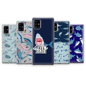 Pu&ograve; includere: Cinque diverse custodie per telefono con un design a squalo. Le custodie sono trasparenti e mostrano una variet&agrave; di motivi di squali, tra cui uno squalo con le parole "Free Kisses" su uno sfondo blu.