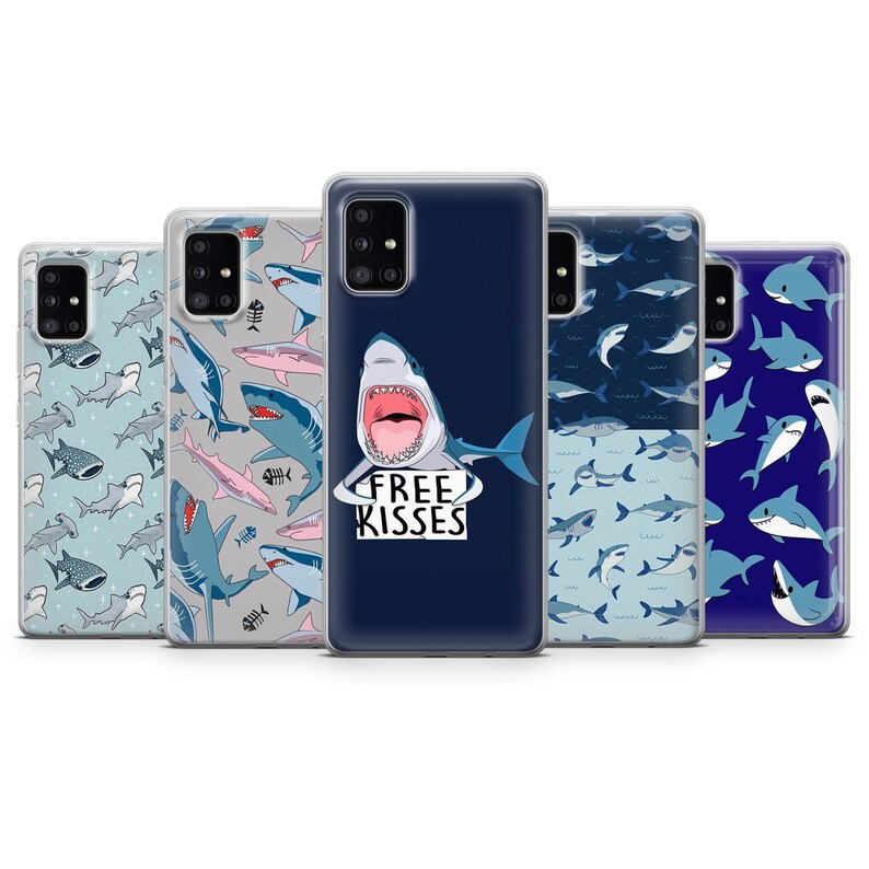 Pu&ograve; includere: Cinque diverse custodie per telefono con un design a squalo. Le custodie sono trasparenti e mostrano una variet&agrave; di motivi di squali, tra cui uno squalo con le parole "Free Kisses" su uno sfondo blu.
