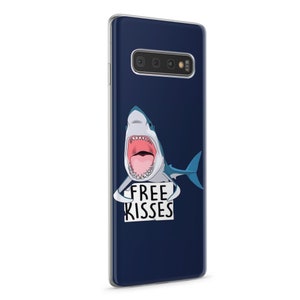 Pu&ograve; includere: Una custodia per telefono blu con uno squalo bianco che tiene un cartello con su scritto "Free Kisses".