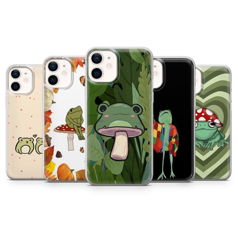 Op de afbeelding: Vijf verschillende telefoonhoesjes met kikkerontwerpen. De hoesjes zijn allemaal transparant en laten het ontwerp van de telefoon eronder zien. De kikkerontwerpen omvatten een kikker op een paddenstoel, een kikker met een hoed, een kikker op een hart en een kikker op een blad.
