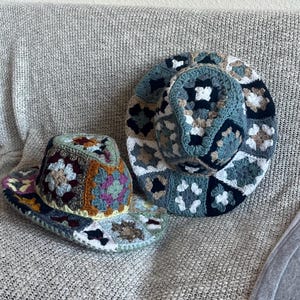 May include: Two handmade crochet hats with wide brims. One hat features a mix of colors including blue, green, brown, and purple. The other hat is primarily blue, white, and brown. Both hats are made with a granny square pattern.