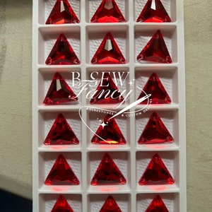 May include: A tray of triangular, faceted, red rhinestones. The rhinestones are arranged in a grid pattern within individual white compartments. The image includes the text "B SEW + Fancy" and "RHINESTONES & CUSTOM DESIGNS".