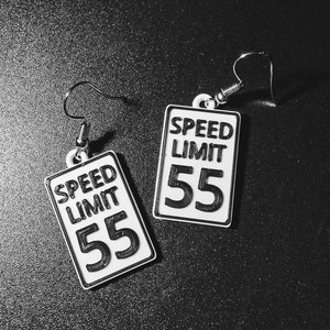 Puede incluir: Un par de pendientes de plata con señales de límite de velocidad blancas. Las señales dicen "Speed Limit 55".