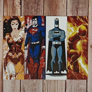 May include: Four rectangular bookmarks featuring DC Comics superheroes: Wonder Woman, Superman, Batman, and The Flash. Each character is depicted in a stylized, comic book art style with vibrant colors and bold outlines. The bookmarks are arranged vertically.