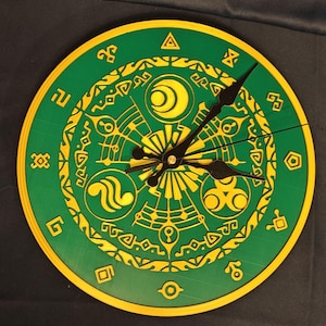 Puede incluir: Un reloj de pared redondo con una esfera verde y un borde amarillo. La esfera del reloj presenta símbolos y diseños amarillos. Las manecillas del reloj son negras. El reloj es un objeto decorativo.