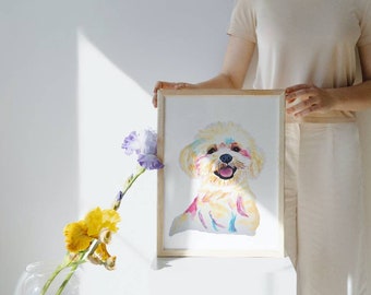 Könnte beinhalten: Ein gerahmtes Aquarellbild eines weißen Hundes mit bunten Akzenten. Der Hund lächelt und hat die Zunge herausgestreckt. Das Bild ist in einem hellen Holzrahmen.