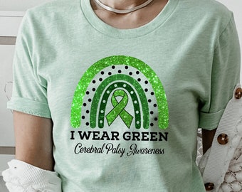 Peut inclure: Un t-shirt vert clair avec un arc-en-ciel vert pailleté et un ruban vert. Le texte "I Wear Green Cerebral Palsy Awareness" est imprimé sur le t-shirt.