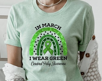 Peut inclure: Un t-shirt vert clair avec un arc-en-ciel vert pailleté et le texte "En mars, je porte du vert pour la sensibilisation à la paralysie cérébrale".