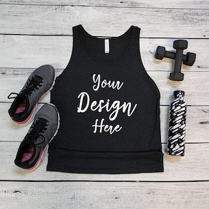 May include: Black tank top with the text "Your Design Here" on a white wood background. The tank top is next to a pair of black running shoes, a water bottle, and a set of black dumbbells.