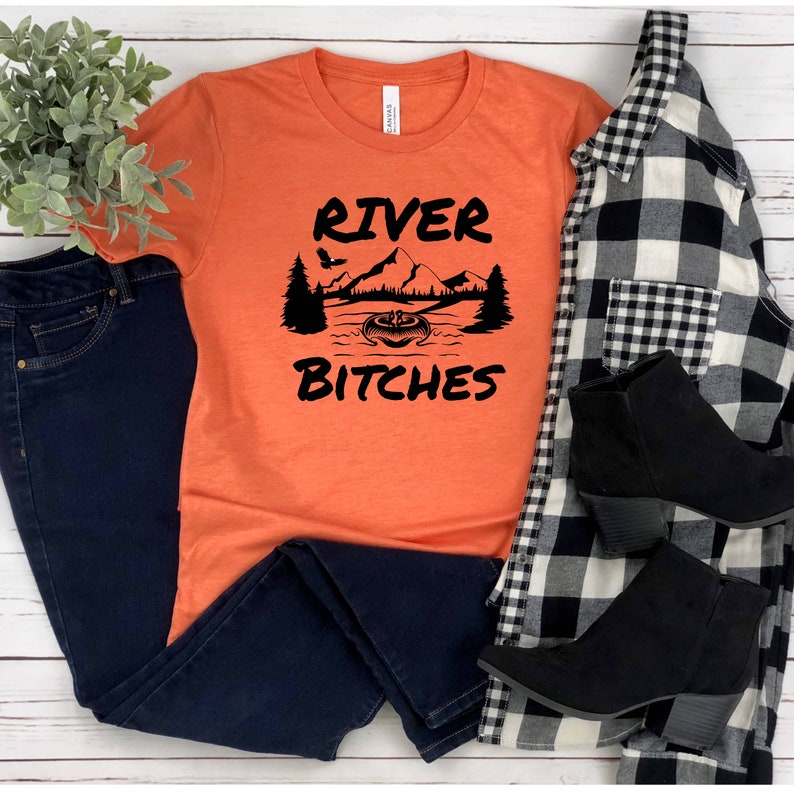 May include: Orange t-shirt with black text that reads "River Bitches" and a graphic of a mountain scene with a boat and a pumpkin.