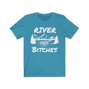 Pu&ograve; includere: Una t-shirt blu turchese con un design grafico bianco di una scena di montagna e il testo "River Bitches".