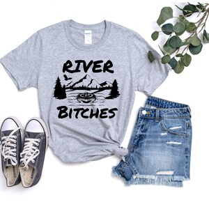 May include: Gray t-shirt with black text that reads "River Bitches" and a graphic of a mountain range, a river, and a canoe.