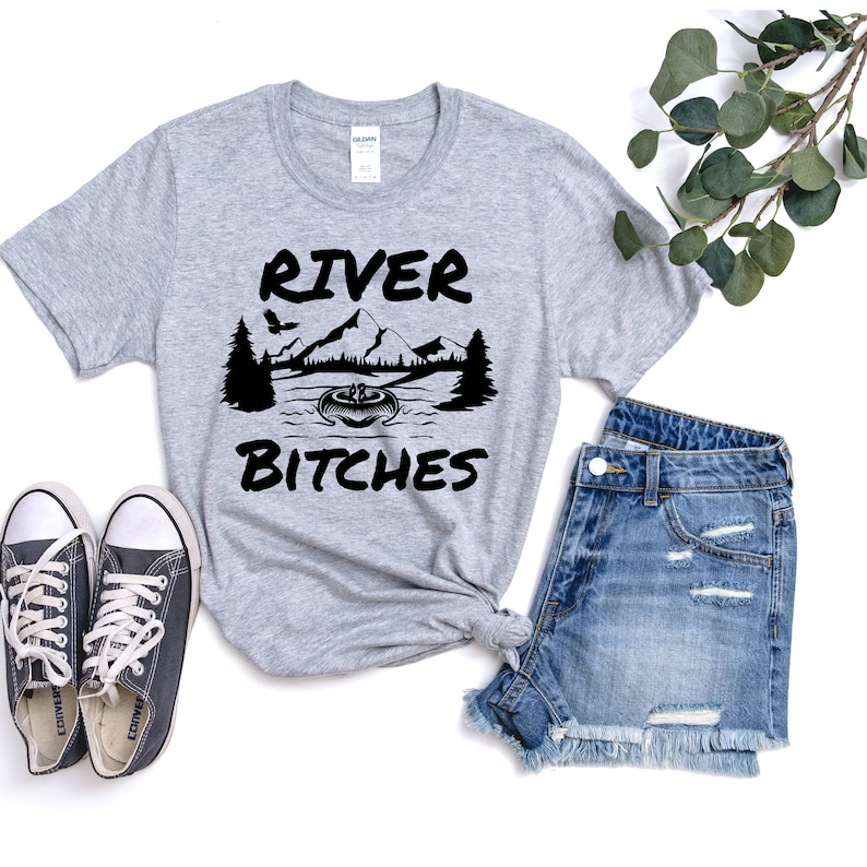 May include: Gray t-shirt with black text that reads "River Bitches" and a graphic of a mountain range, a river, and a canoe.