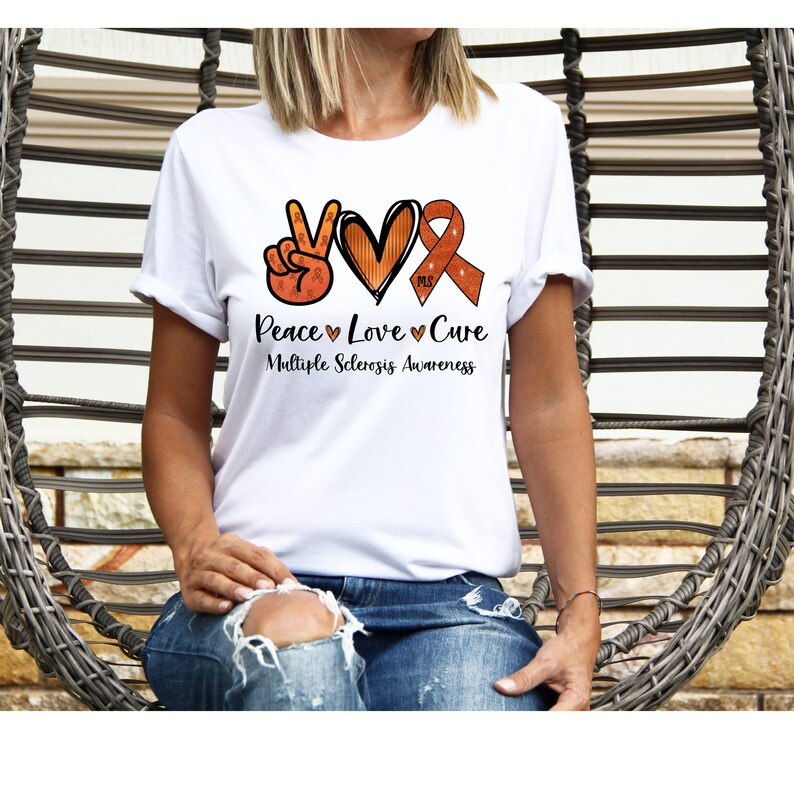 Puede incluir: Camiseta blanca con un signo de paz, un coraz&oacute;n y una cinta naranja con el texto "Peace Love Cure Multiple Sclerosis Awareness".