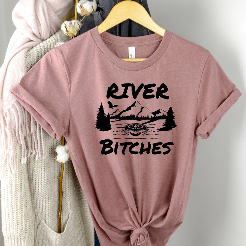 May include: A pink t-shirt with a black graphic design that says "River Bitches" with a mountain and river scene.