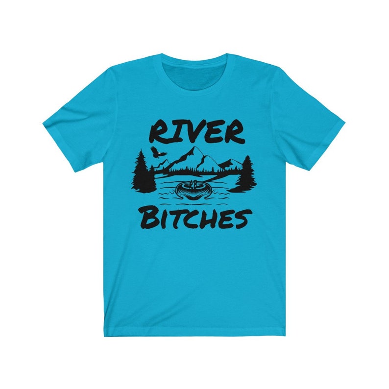 May include: A turquoise blue t-shirt with a black graphic design of a river scene with mountains, trees, and a boat. The text "River Bitches" is printed on the shirt.