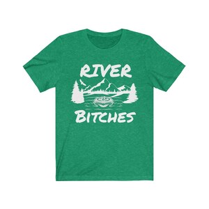 Pu&ograve; includere: Maglietta verde con testo bianco che dice "River Bitches" e una grafica di una scena di fiume con montagne e alberi.