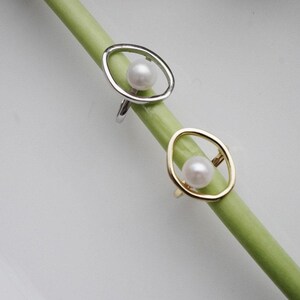 Puede incluir: Dos anillos con una perla en el centro. El anillo de la izquierda es de plata y el anillo de la derecha es de oro.