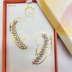 May include: Ear cuffs with iridescent gemstones arranged in a curved line, presented in a box. The box is peach-colored with the words "EAR CUFF" and the brand "C&C California". The box lid has a watercolor design.
